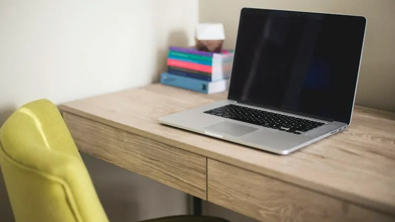 A laptop and books on a wooden desk beside a green chair